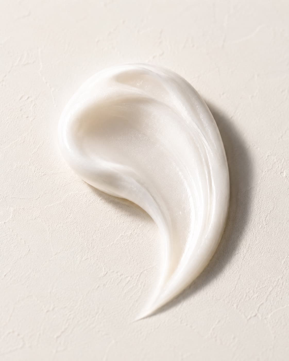 Smooth cream swept into flowing shapes on an ivory surface in warm light